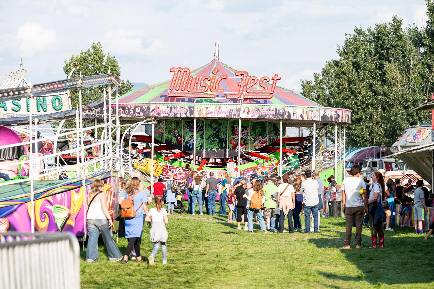 Crowds of fairgoers gathered around colorful carnival rides on a sunny day at the Ravalli County Fair and Rodeo in Hamilton, Montana