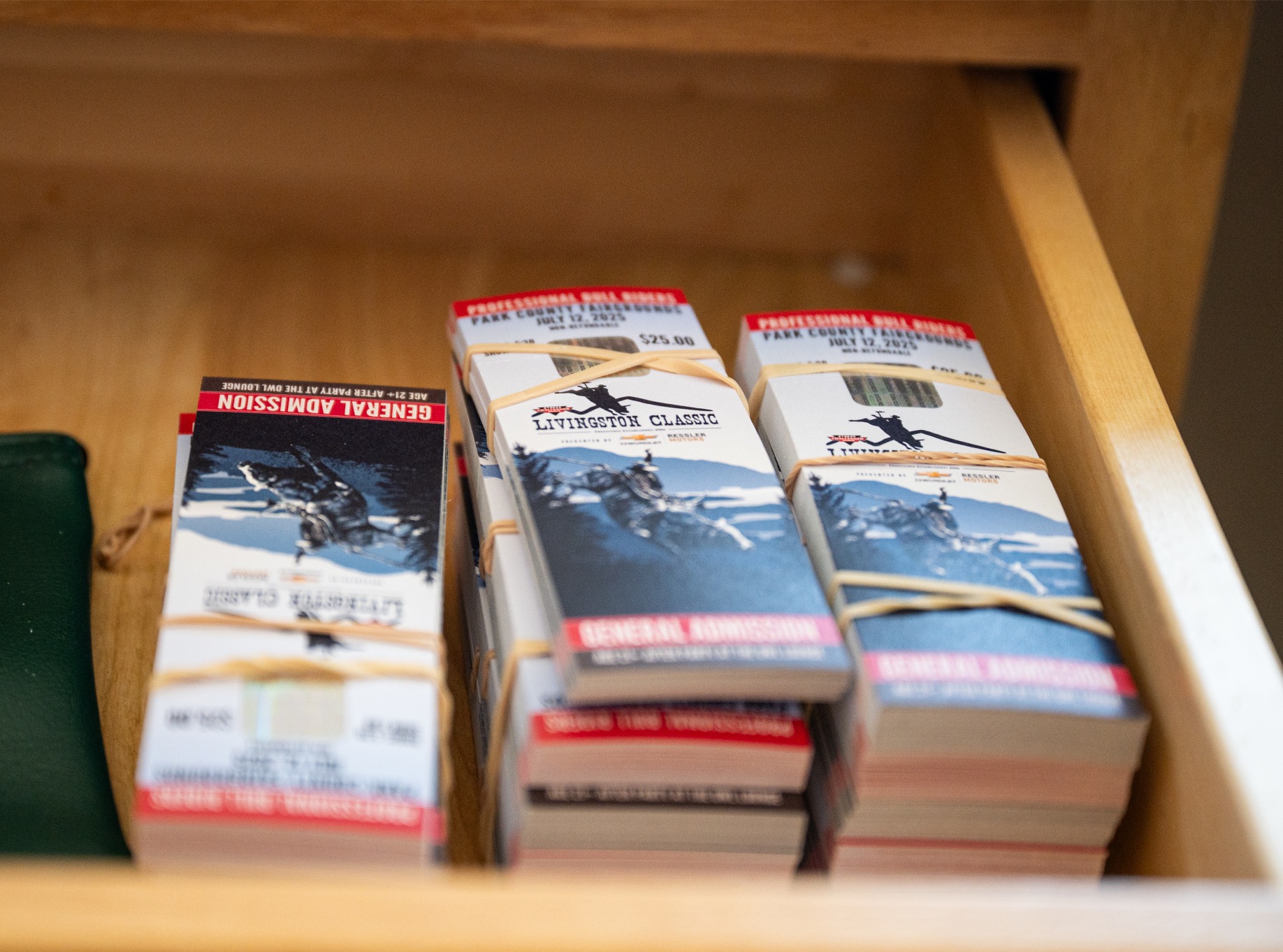 general-admission-tickets-rodeo-event Three bundled stacks of printed general admission tickets for the Livingston Classic rodeo event, sitting in a wooden drawer at the venue.